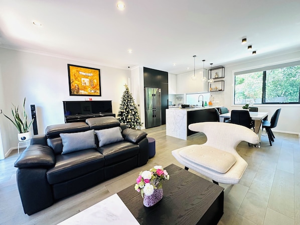 A modern living room with a black leather sofa, a white coffee table, and a Christmas tree.