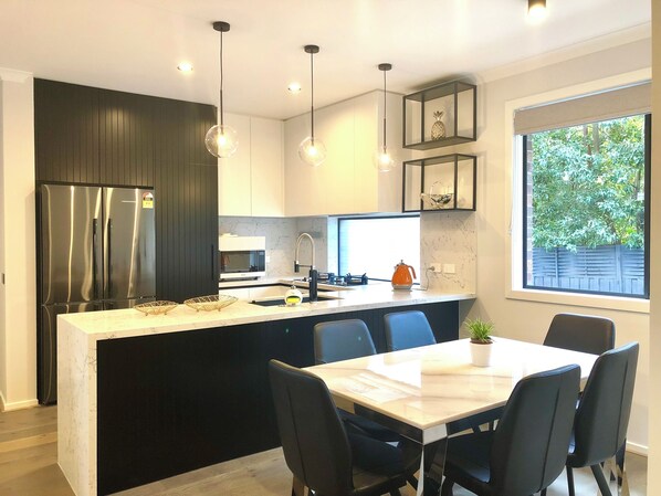 A modern kitchen with a central island, black cabinets, stainless steel appliances, and pendant lighting.