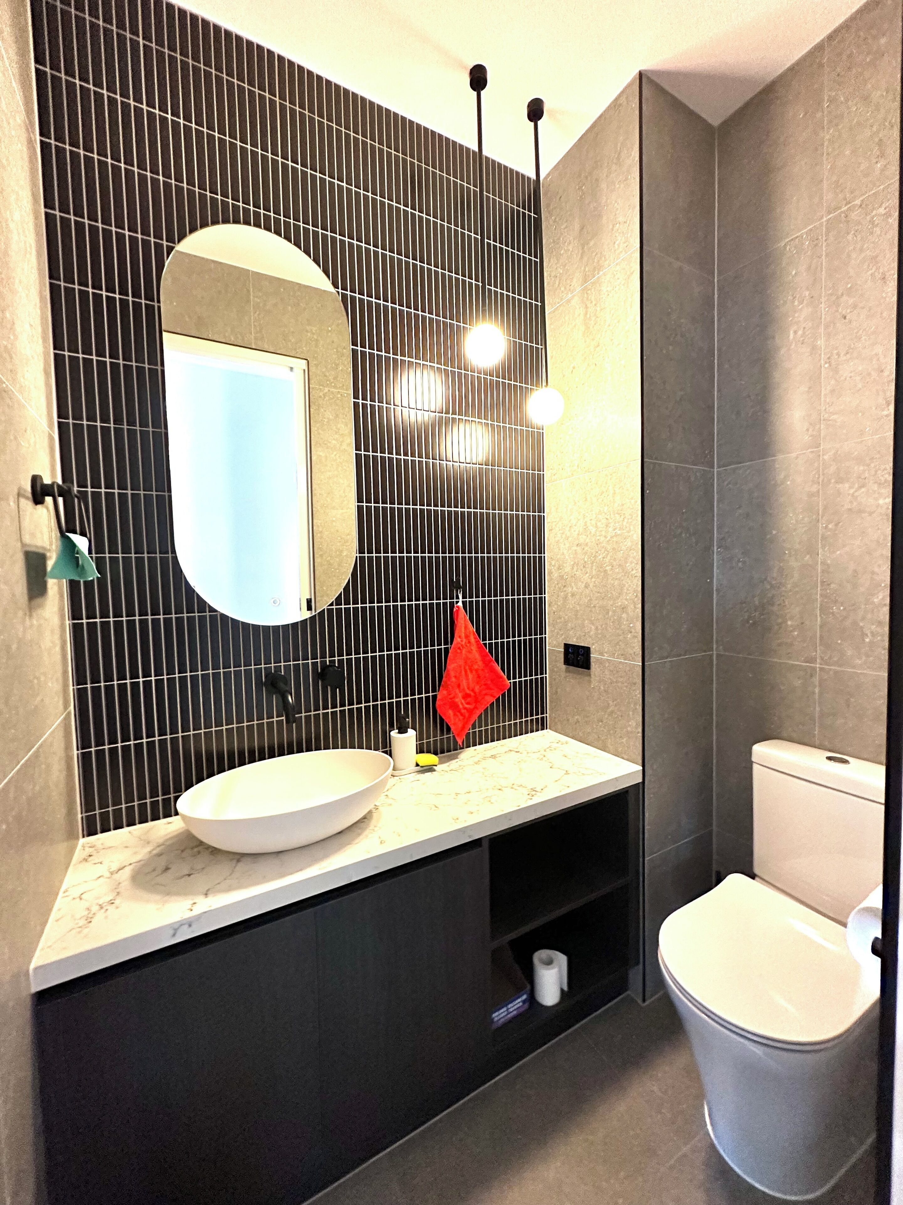 A modern bathroom with a large mirror, a white sink, and a toilet.