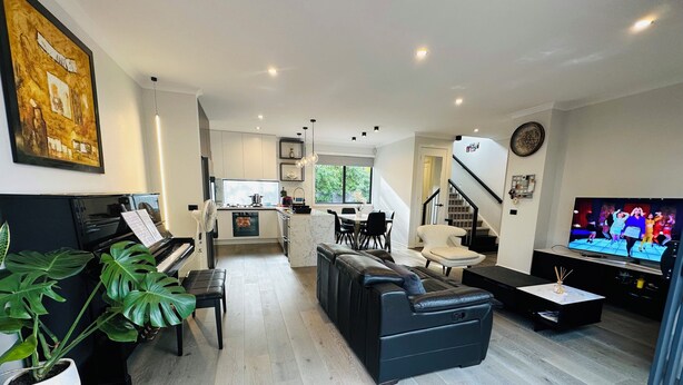 Una sala de estar moderna con un piano, sofá de cuero negro y un televisor.