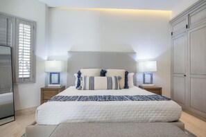 Quarto com uma cama grande, duas mesas de cabeceira com luminárias, um guarda-roupa e uma janela com persianas.