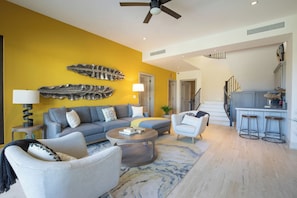 Uma sala de estar com sofá, poltronas, mesa de centro e um espaço de jantar com banquetas.