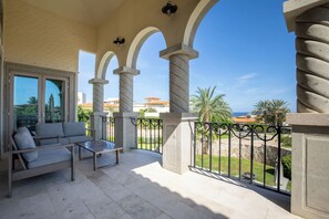 Ein Balkon mit einer Couch und einem Tisch, Stein Säulen und Blick aufs Meer.