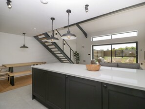Una cocina moderna con una isla grande, iluminación colgante y vistas al jardín trasero.