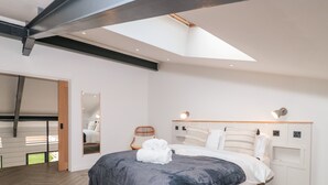 Ett modernt sovrum med en stor säng, en sänggavel i trä, en spegel och ett takfönster.