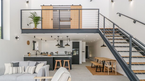 En modern lägenhet i loftstil med en övre våningsplan, öppet kök, matplats och en trappa.