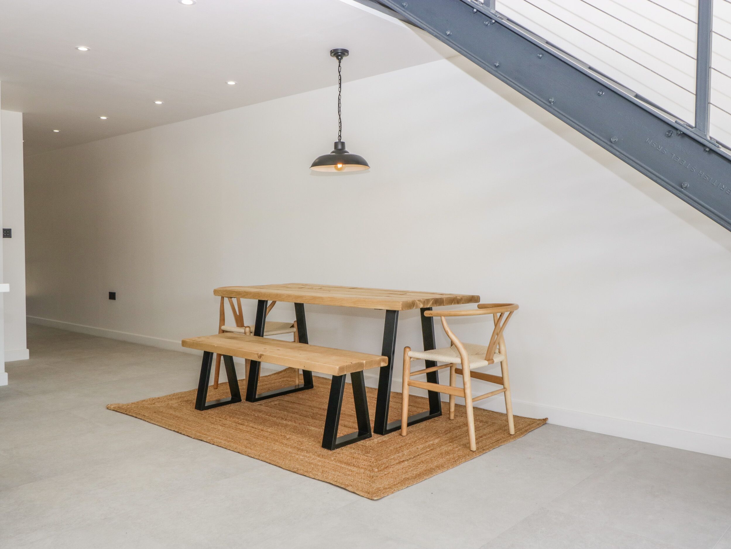 A dining area with a wooden table and benches, a hanging light fixture, and a staircase in the background.