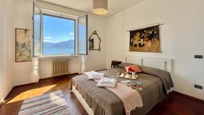Un dormitorio con un ventanal grande, una cama, una mesita de noche y un radiador.