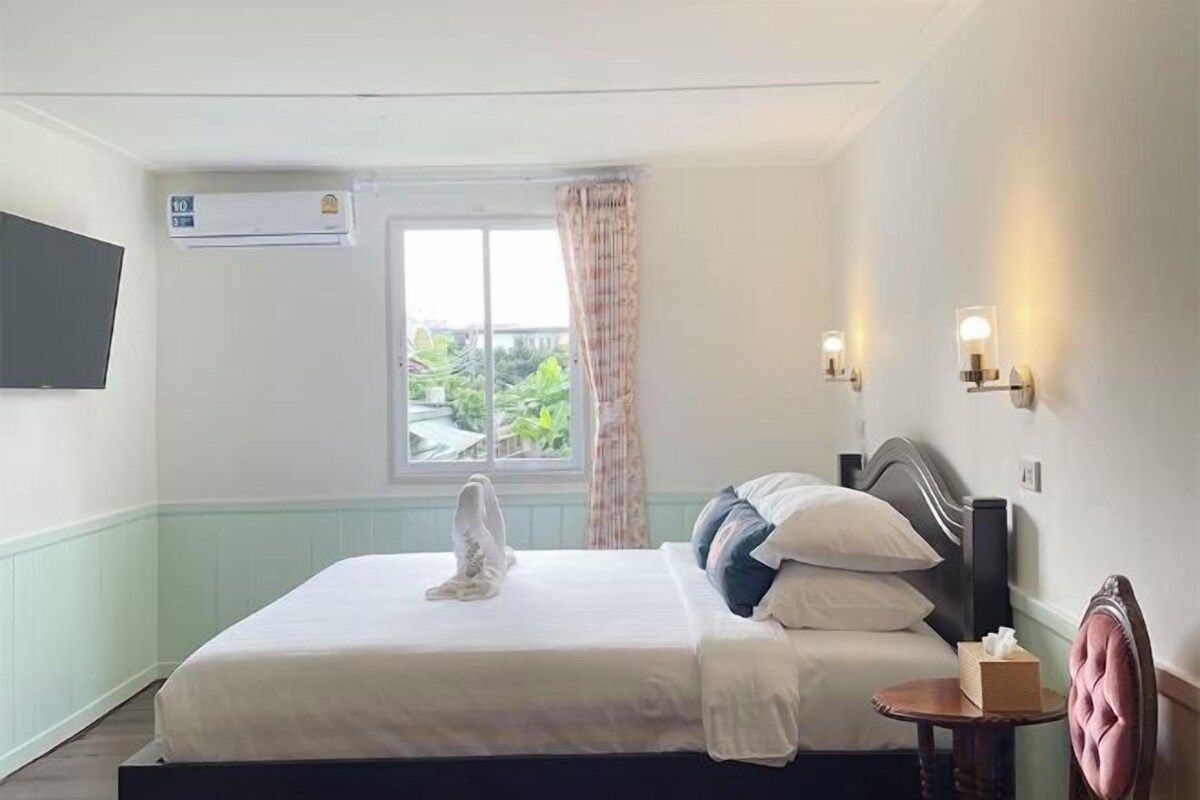 Une chambre d’hôtel avec un lit, une fenêtre avec un rideau, un téléviseur fixé au mur et une table de chevet avec une lampe.