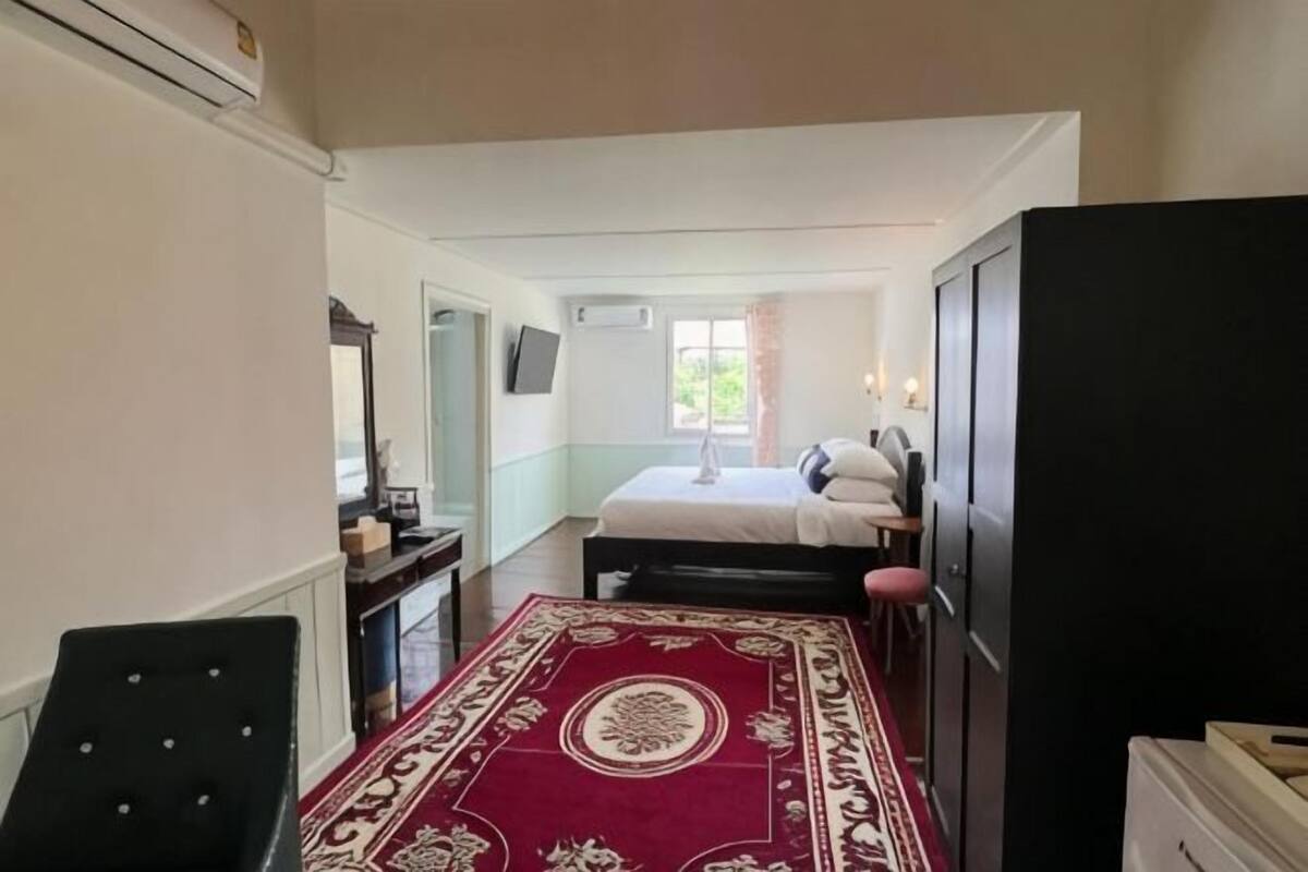 A bedroom with a bed, a desk, a chair, a TV, and a window.