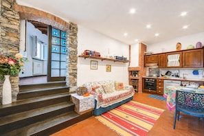 A cozy living room with a sofa, a dining table, and a kitchen area with wooden cabinets and a brick wall. - La Stalletta Relax - With Private Parking (Alassio)