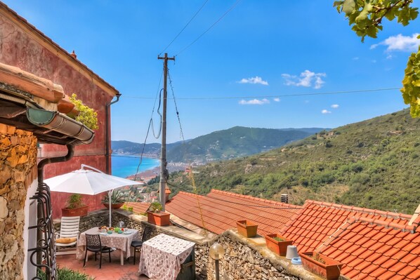 A terrace with a table and chairs, potted plants, and a view of the sea.