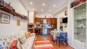 Uma sala de estar acolhedora com um sofá, uma mesa de jantar com cadeiras, uma cozinha com armários e eletrodomésticos, e uma vitrine de vidro.