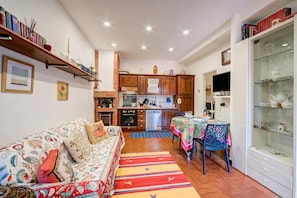 A cozy living room with a sofa, a dining table with chairs, a kitchen area with cabinets and appliances, and a glass display cabinet.