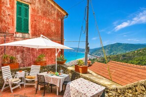 A terrace with a table, chairs, and potted plants, overlooking a coastal landscape.
