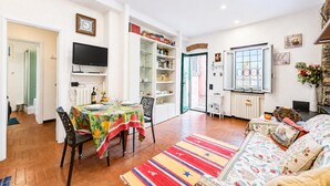 Uma sala de estar com sofá, mesa de jantar e cadeiras, televisão e estante de livros.
