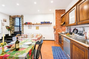 A kitchen with wooden cabinets, a brick wall, a dining area with a table set for two, and a built-in oven. - La Stalletta Relax - With Private Parking (Alassio)