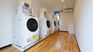 A row of white front-loading washers in a hallway with wooden flooring and white walls. - HOTEL R9 The Yard Iwakuni (Iwakuni)