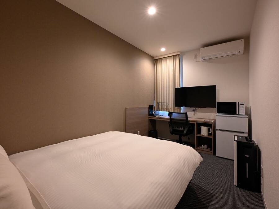 Une chambre d’hôtel équipée d’un lit, d’un bureau avec un ordinateur, d’une télévision et d’un appareil de climatisation.
