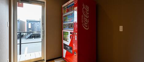 A Coca-Cola vending machine in a room with wooden flooring and a door leading outside.