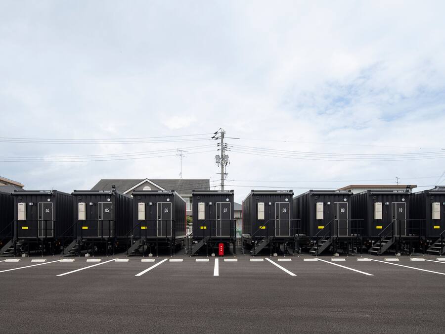 A row of black portable toilets with white doors and numbered from 03 to 11, arranged in a parking lot with white lines marking parking spaces.