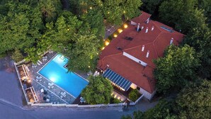 Vista aérea de una propiedad con piscina, un edificio de techo rojo y un puente de piedra sobre un río.