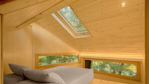 Un dormitorio con tragaluces, una cama con almohadas y ventanas con vistas a árboles.