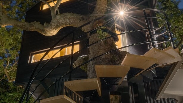 Una casa en árbol con varios niveles conectados por escaleras de madera, rodeada de exuberante vegetación.