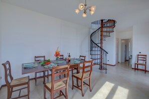 A dining area with a wooden table, chairs, and a chandelier. There is a spiral staircase to the right.