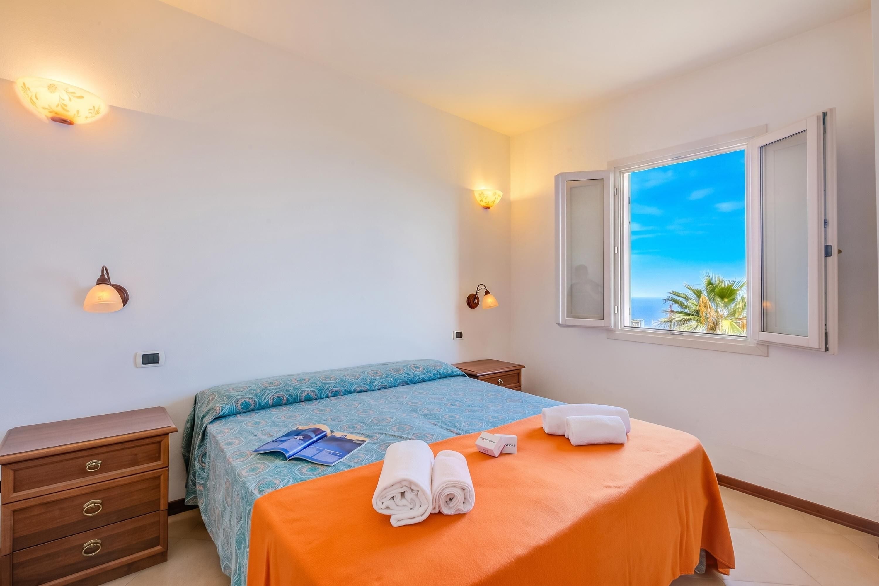 Quarto de hotel com cama, mesa de cabeceira, cômoda e janela com vista para o mar.