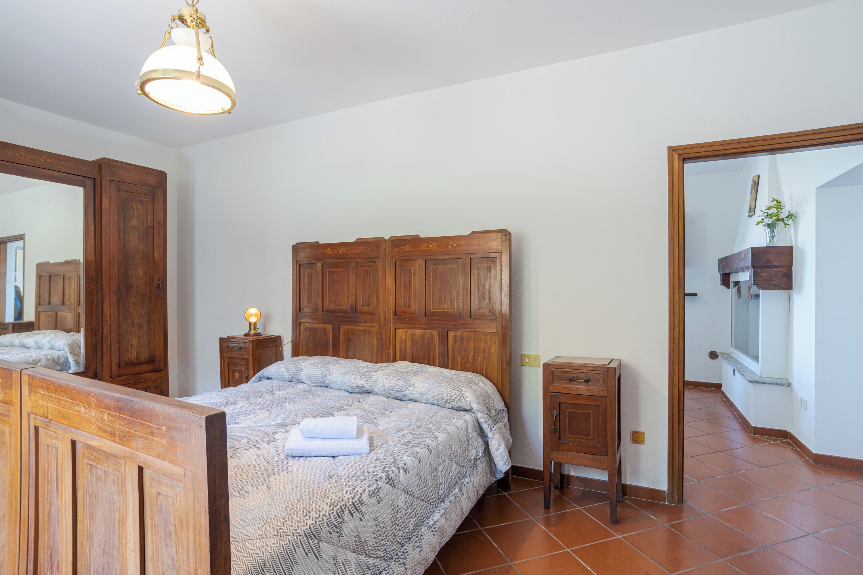 A bedroom with a wooden bed, a nightstand, a dresser, and a large mirror.