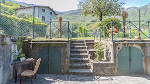A stone staircase leading to a gated entrance, a wicker chair, and a table with a vase and books. - Casa Achille Pianello (Pianello del Lario)