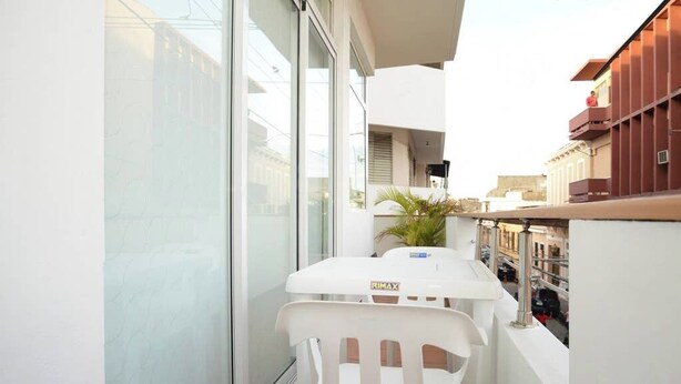 A balcony with a white table and chair, a potted plant, and a view of the street below.