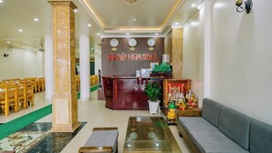A hotel lobby with a reception desk, seating area, and a green carpet leading to a dining area. - Gia Cat Long Hotel (Hai Phong)