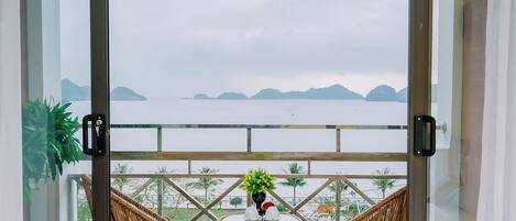 A balcony with wicker chairs and a small table, overlooking a calm sea and distant islands.
