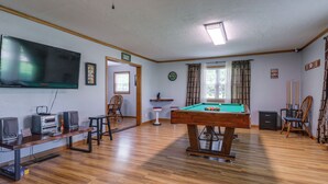 Una habitación con mesa de billar, televisor, altavoces y soporte para billares.
