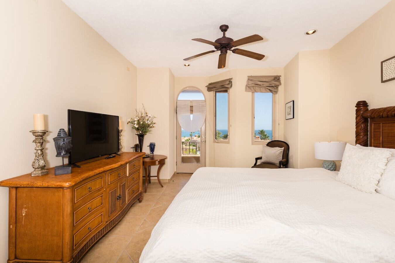 A bedroom with a large bed, a wooden dresser, a television, and a ceiling fan.