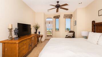 A bedroom with a large bed, a wooden dresser, a television, and a ceiling fan.