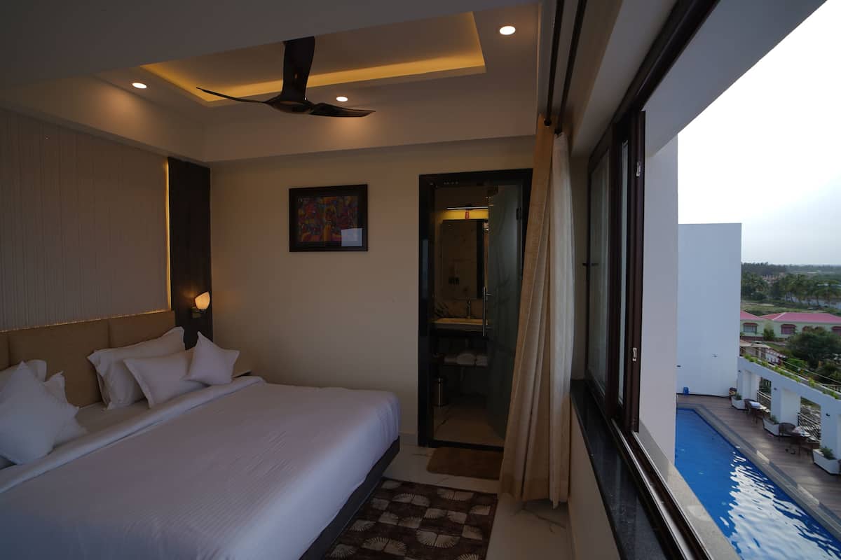 A hotel room with a bed, a ceiling fan, a painting, and a view of a swimming pool.