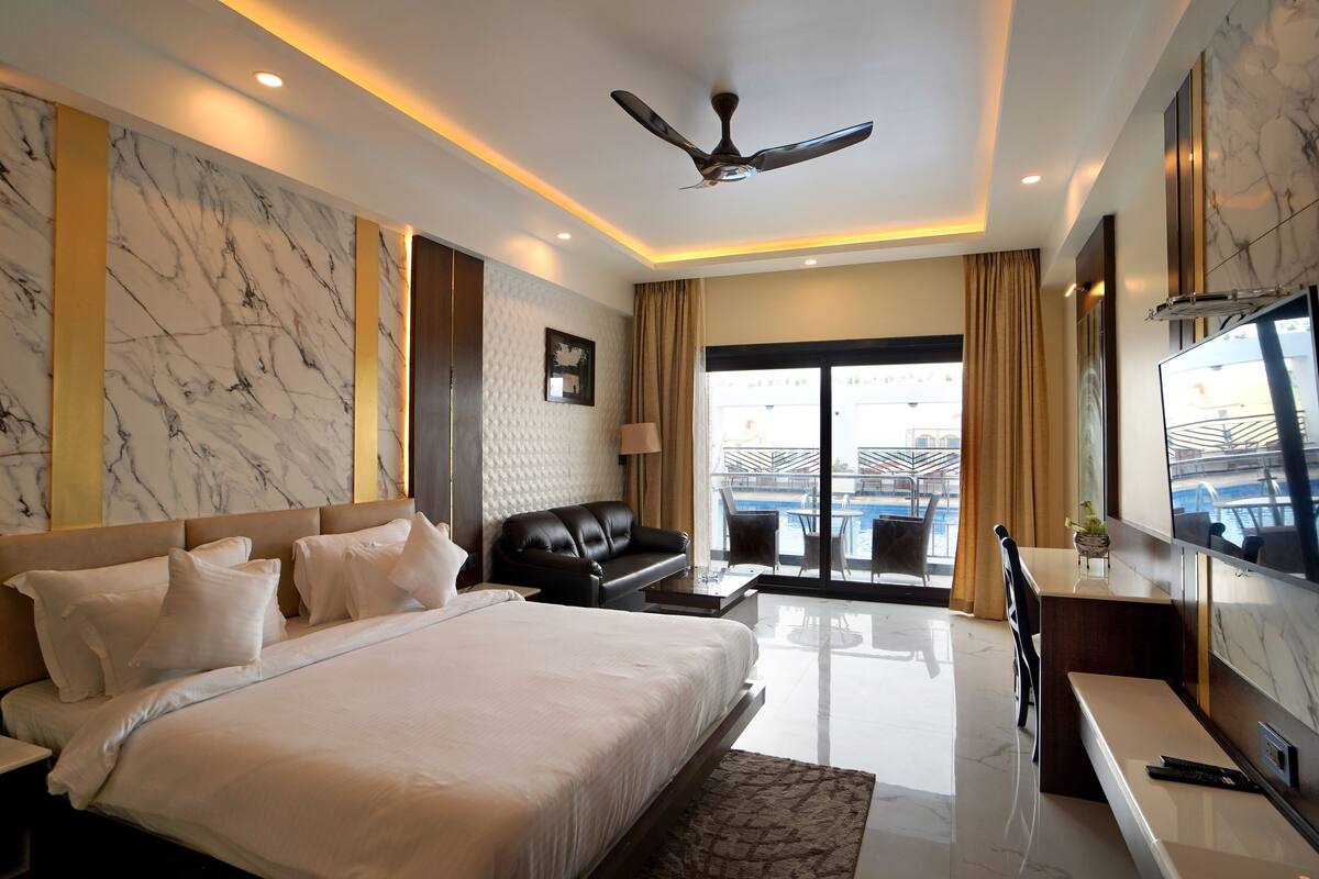 A modern hotel room with a large bed, a flat-screen TV, a ceiling fan, and a view of the pool area.