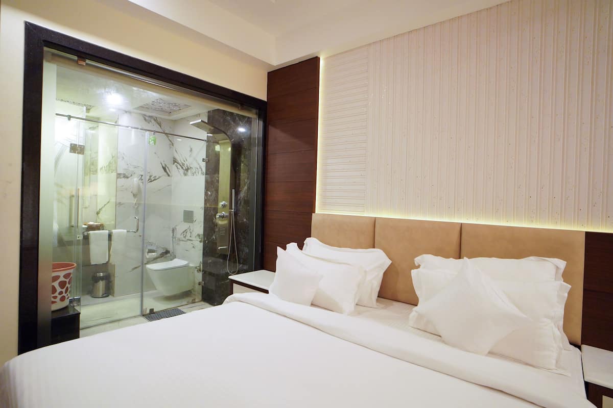 A hotel room with a bed, a glass shower enclosure, and a wooden headboard.
