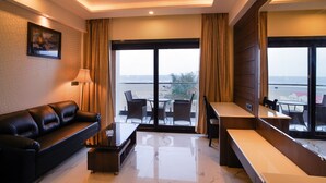 A modern hotel room with a leather sofa, a small table, a chair, and a balcony with a view of the sea. - Shanti seaview resort and spa (Kanthi)