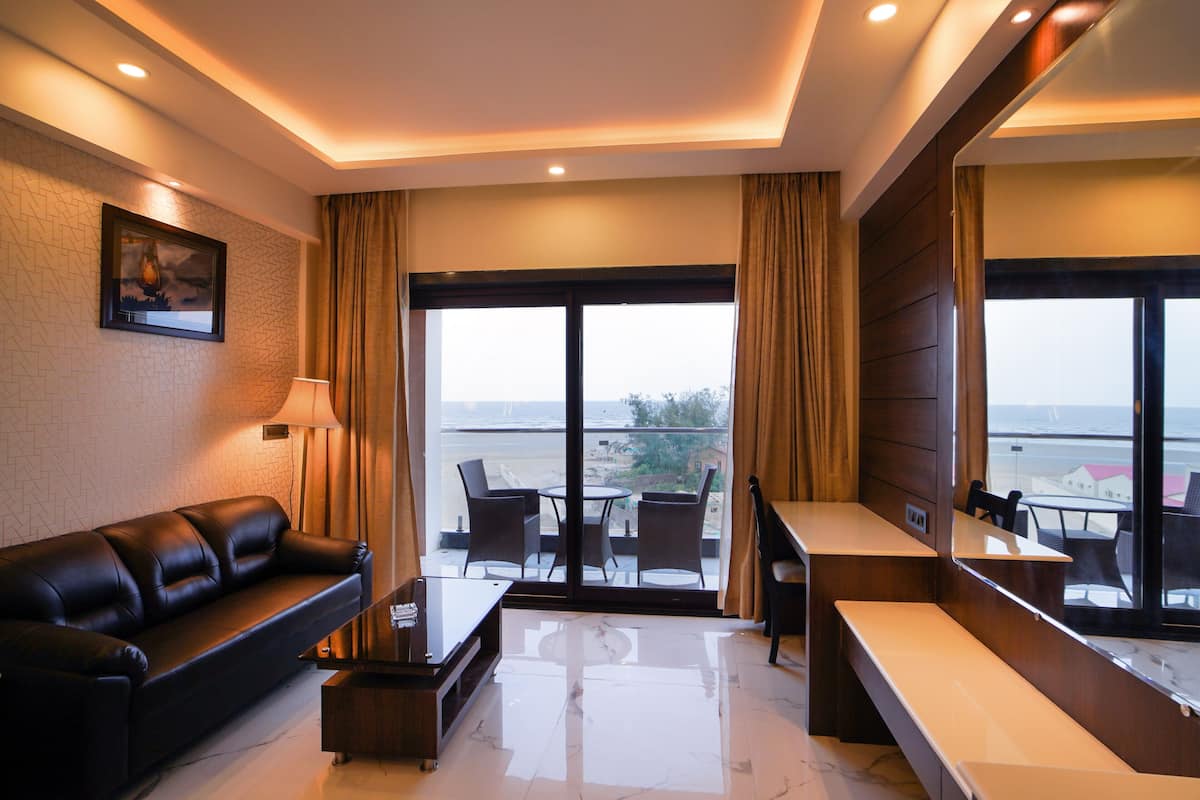 A modern hotel room with a leather sofa, a small table, a chair, and a balcony with a view of the sea.