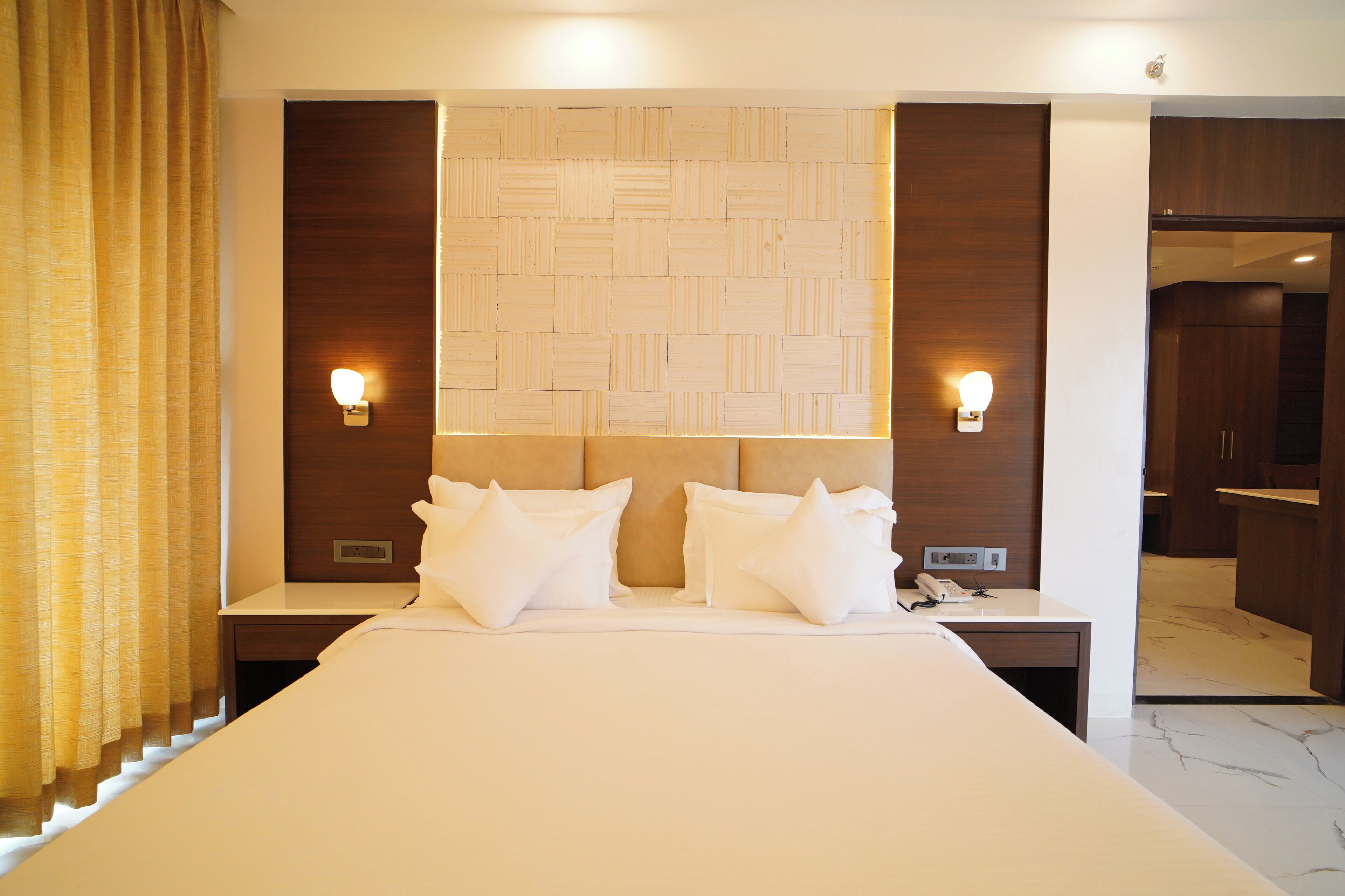 Une chambre d’hôtel avec un grand lit, deux tables de chevet, une tête de lit ornée d’un motif géométrique et deux appliques murales.