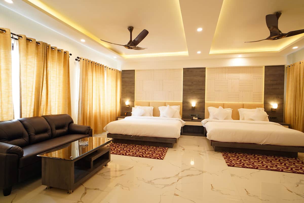A hotel room with two beds, a sofa, a coffee table, and a ceiling fan.