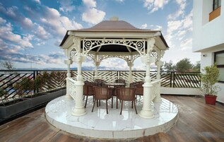 Un belvédère doté d’un toit blanc et d’une décoration raffinée, entouré de chaises en osier et d’une table blanche, installé sur un balcon offrant une vue sur la mer.