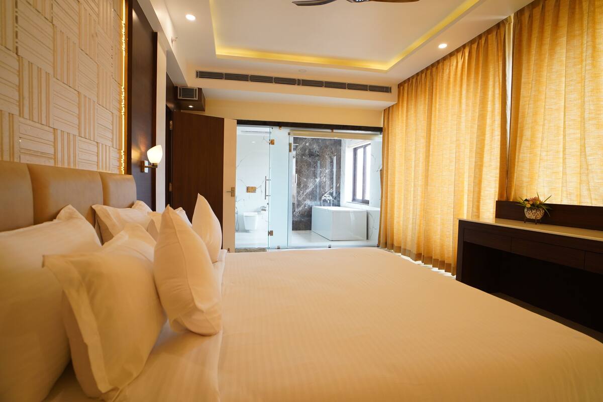 A modern hotel room with a large bed, a TV, and a view of the bathroom and balcony.