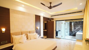 A modern hotel room with a large bed, a ceiling fan, and a glass door leading to a balcony. - Shanti seaview resort and spa (Kanthi)