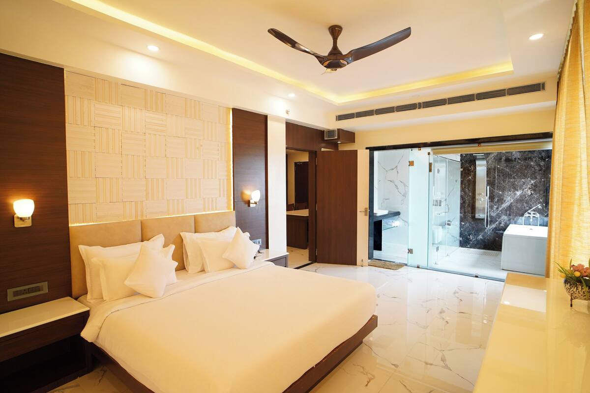 A modern hotel room with a large bed, a ceiling fan, and a glass door leading to a balcony.