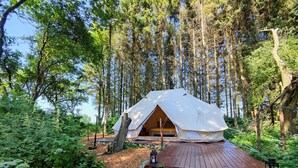 A dome-shaped tent with a wooden deck, surrounded by a forest. - Under Canvas Bornholm (Østermarie)